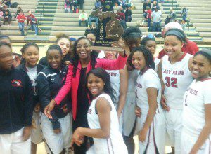 Muskegon head coach Taushauna Burrel holds aloft the girls district title trophy, the school's first such title since 2002 and just its second overall. Photo/Mark Lewis